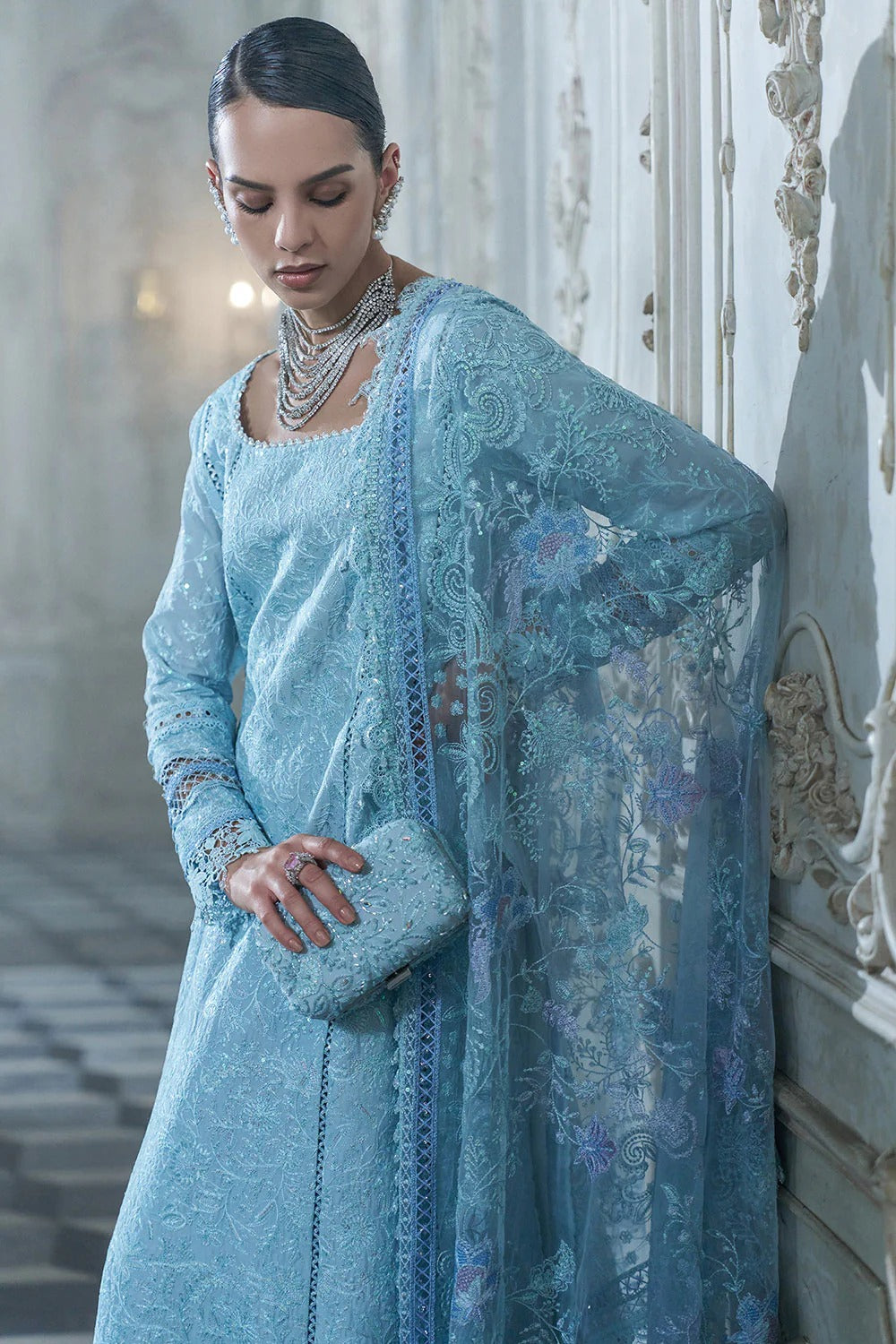 Woman wearing a light blue embroidered traditional outfit in an elegant interior setting.
