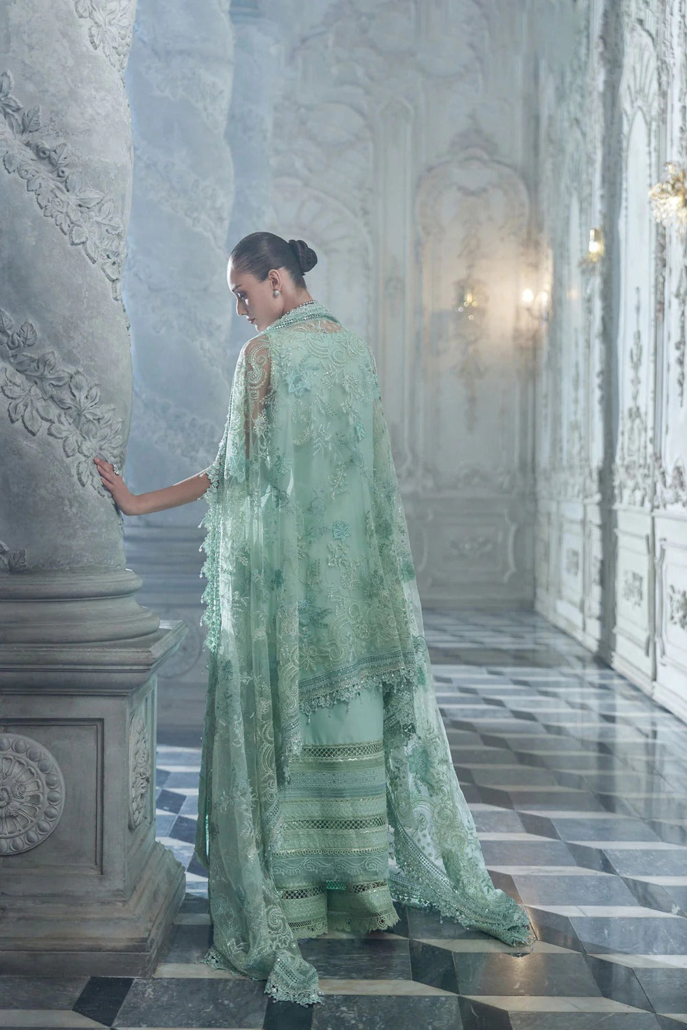 Woman in a light green traditional outfit standing on a marble staircase.