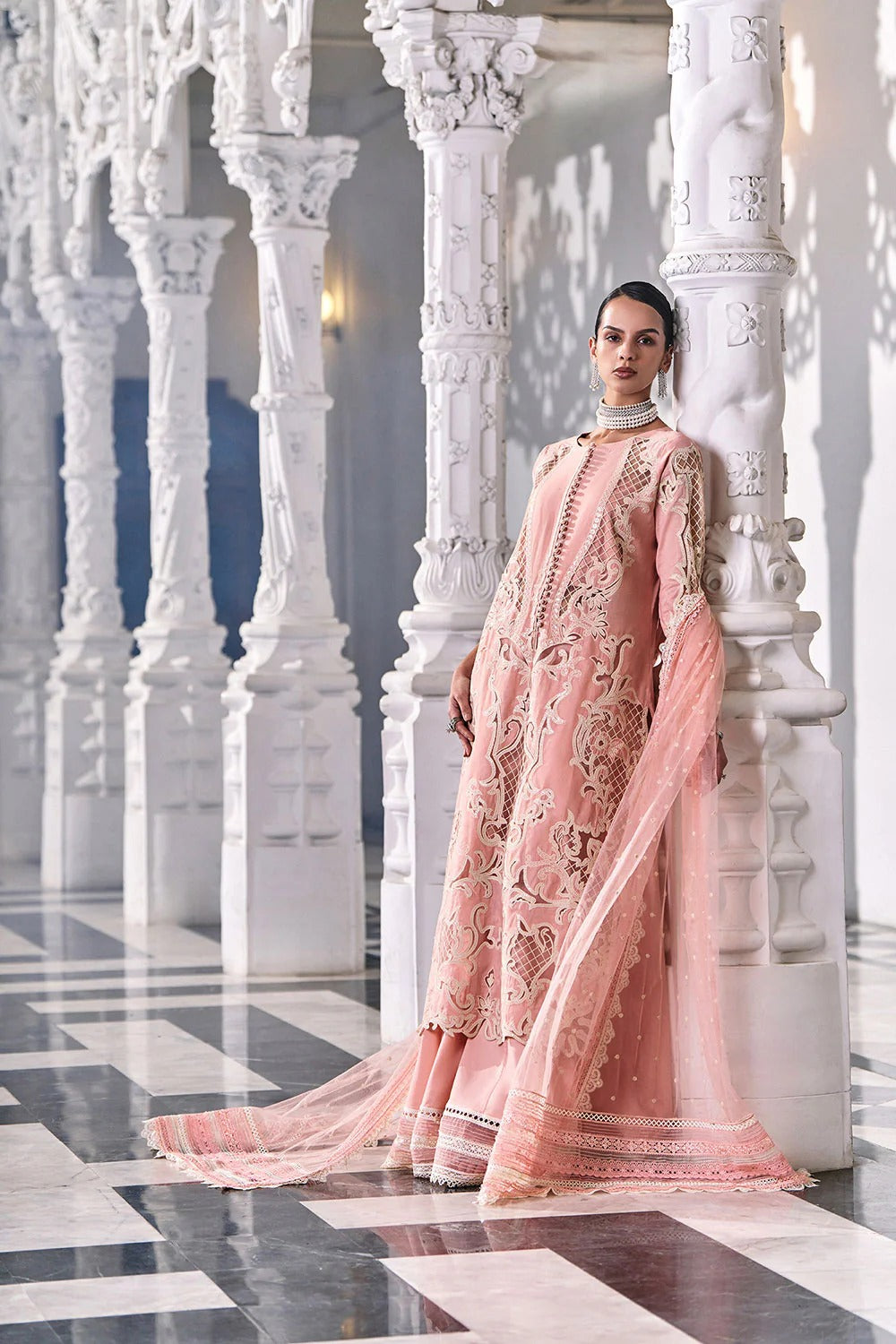 Woman in a pink traditional outfit standing in an elegant interior setting with white marble columns.