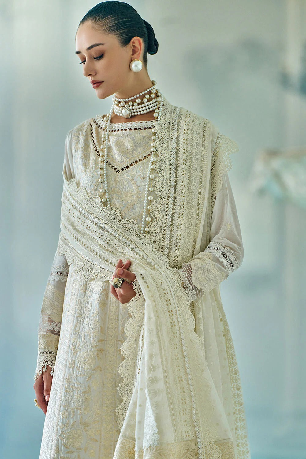 Woman wearing an elegant white embroidered outfit with jewelry against a light background