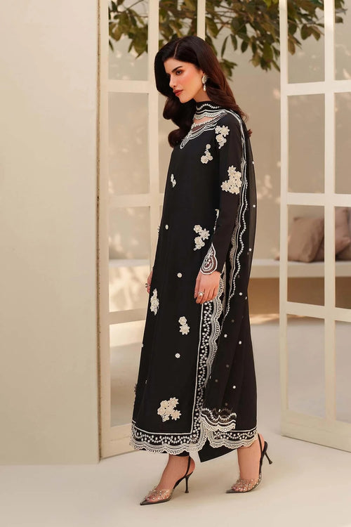 Woman wearing a black embroidered outfit with white patterns in a minimal indoor setting.