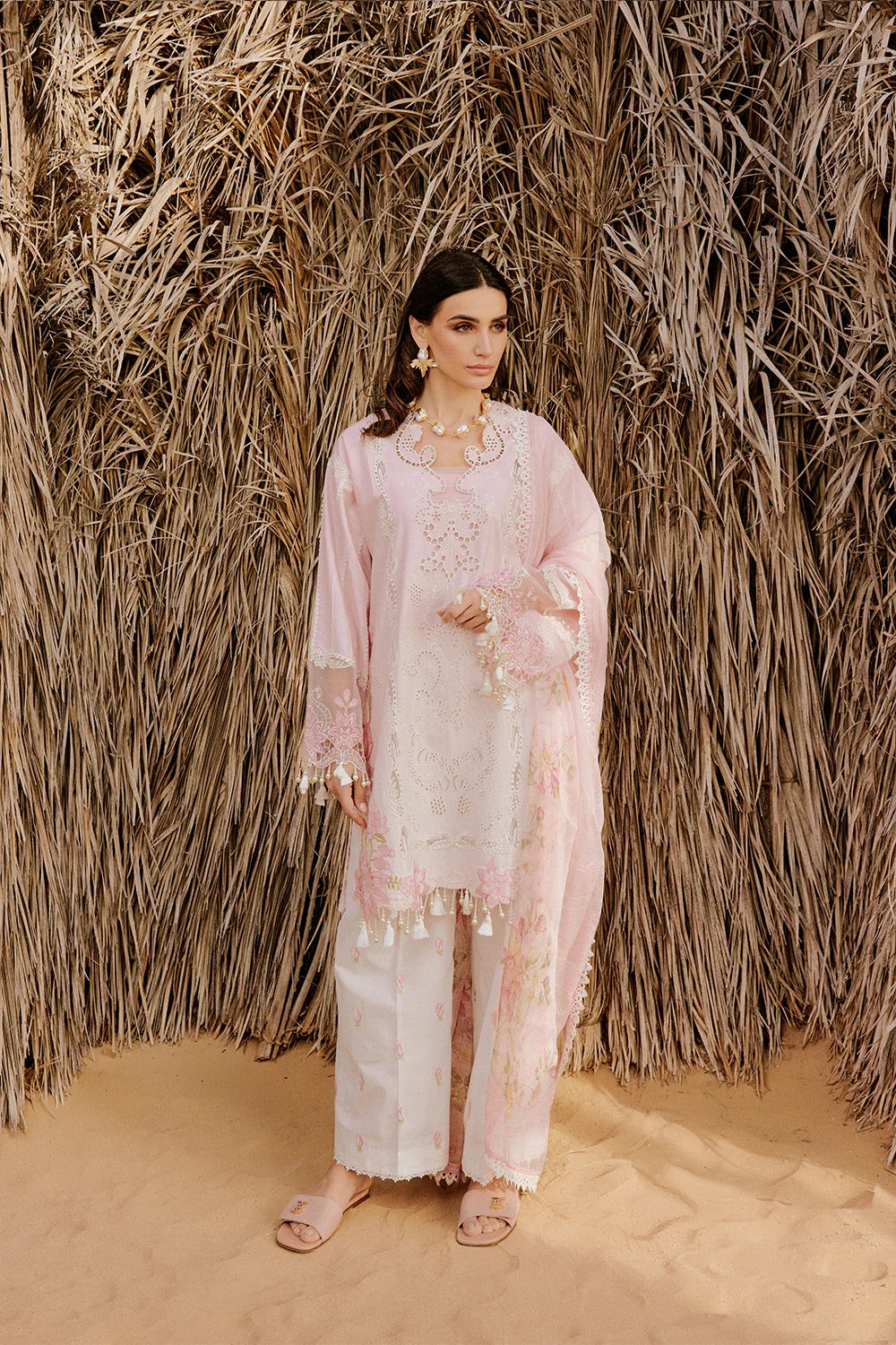 Woman in a light pink and white traditional outfit standing against a textured wall.