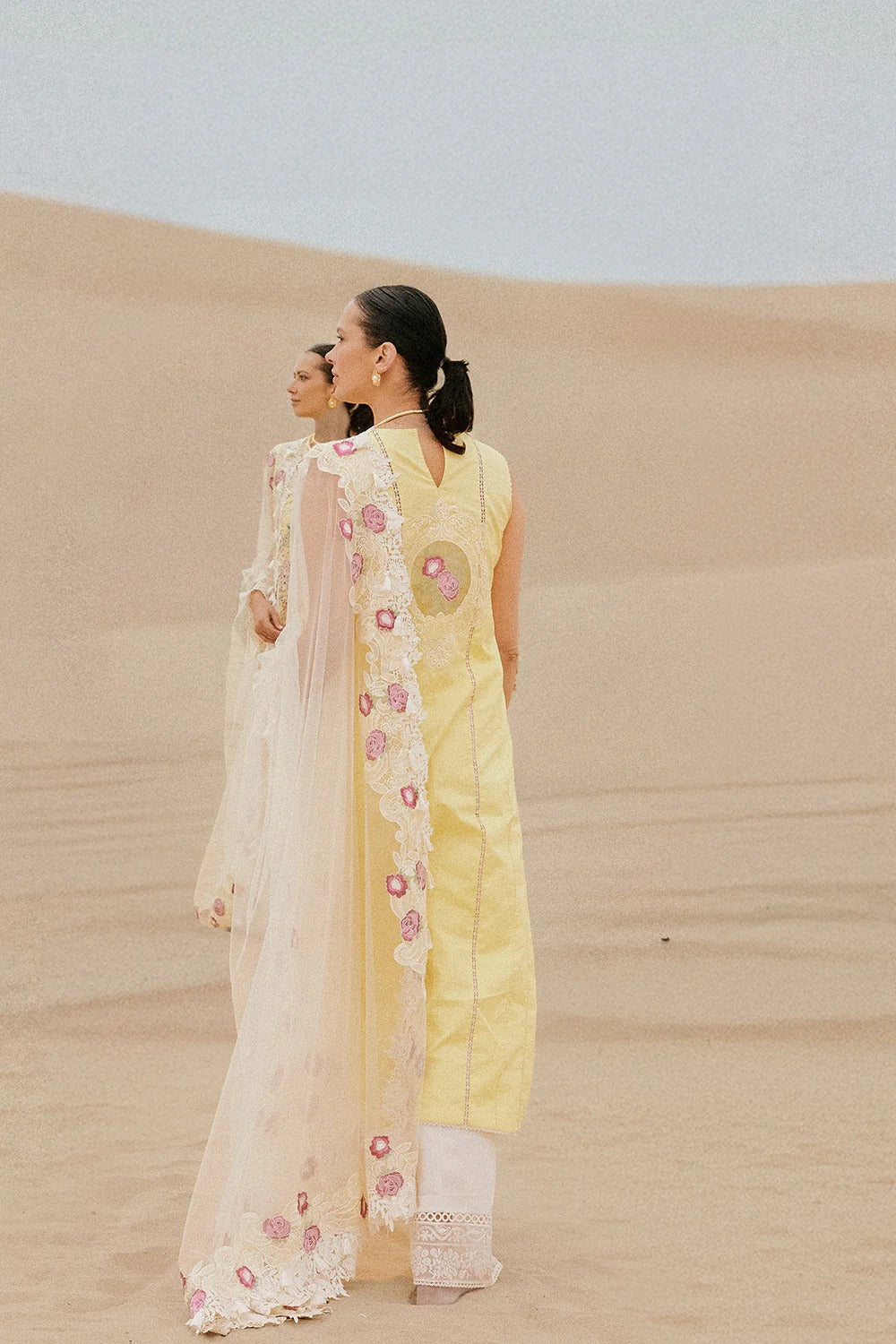 Woman in a yellow floral dress standing on sand dunes