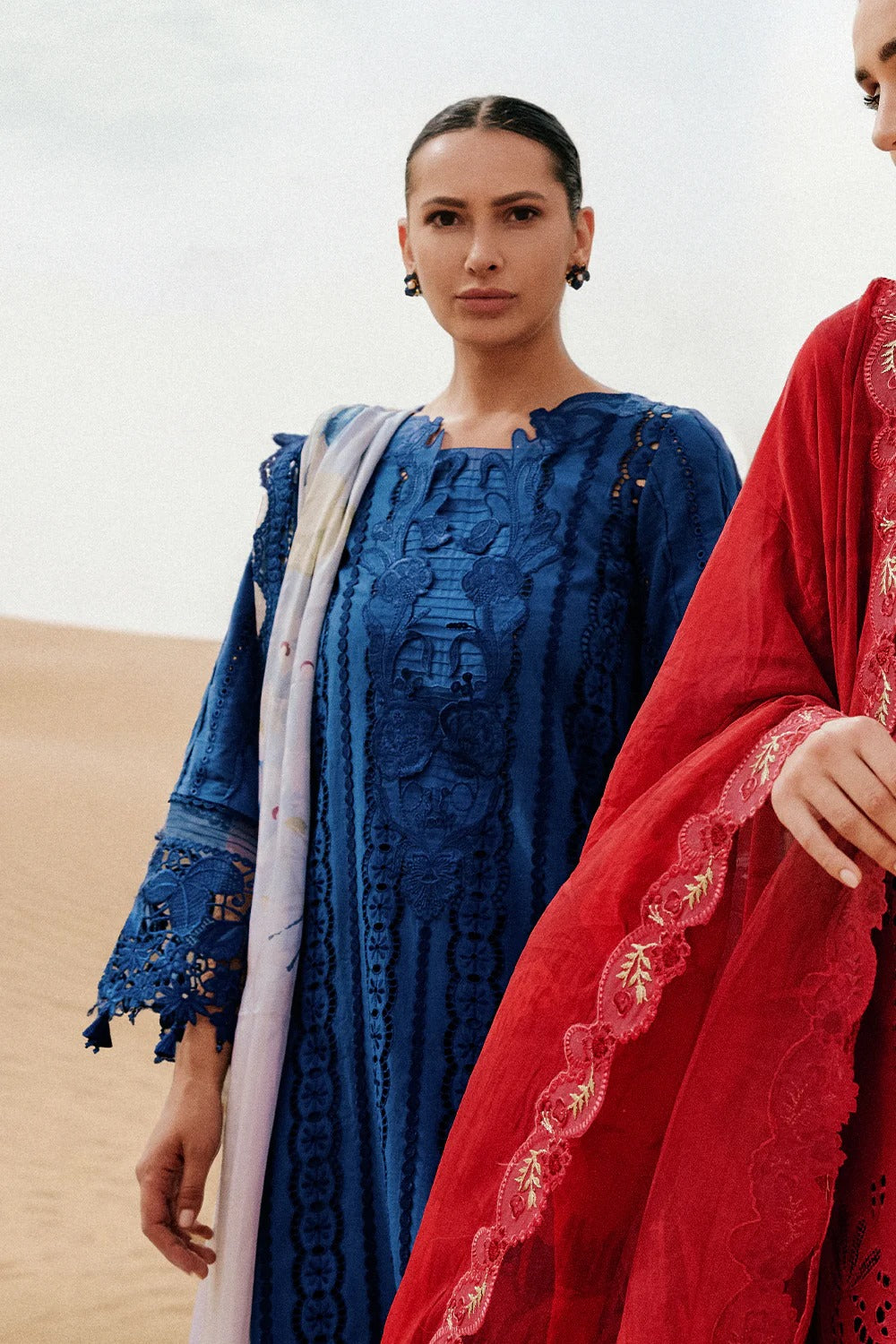 Two women in traditional embroidered dresses standing in a desert setting.
