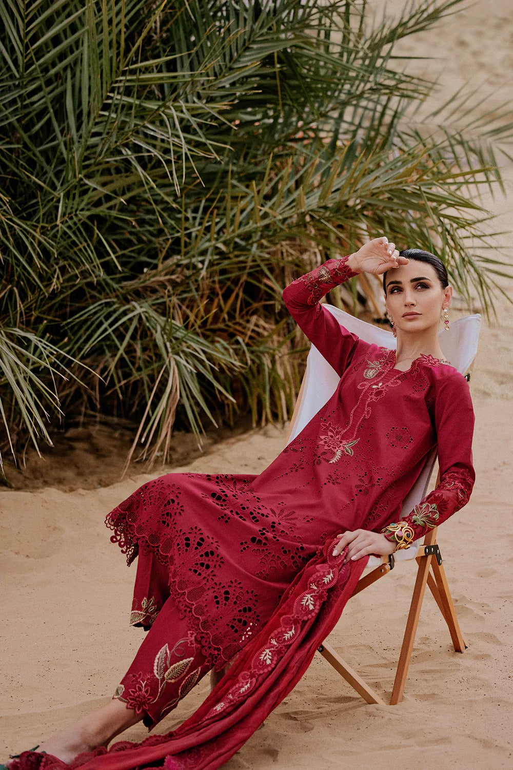 Woman in a red embroidered dress sitting on a chair in a desert setting with greenery.