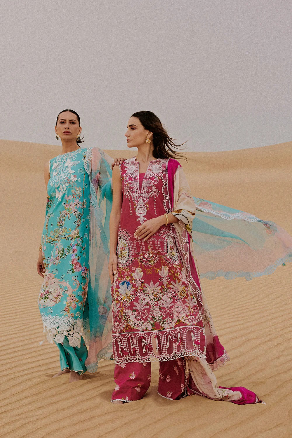 Two women in traditional embroidered dresses standing on sand dunes.