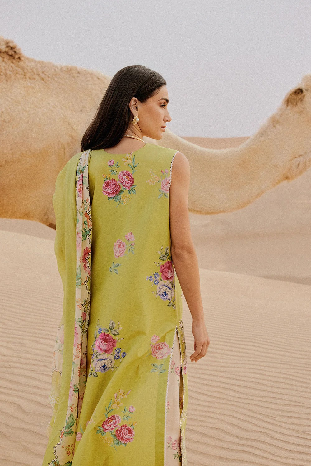 Woman in a yellow floral dress standing next to a camel in a desert setting