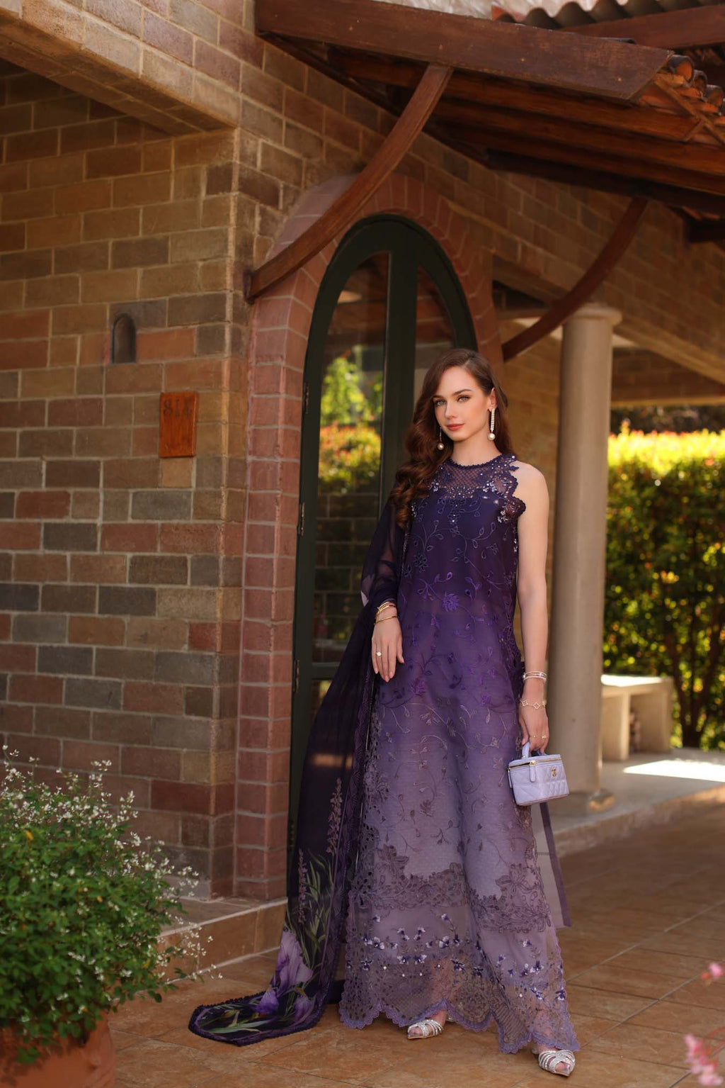Woman in a purple dress standing in front of a brick building with an archway.