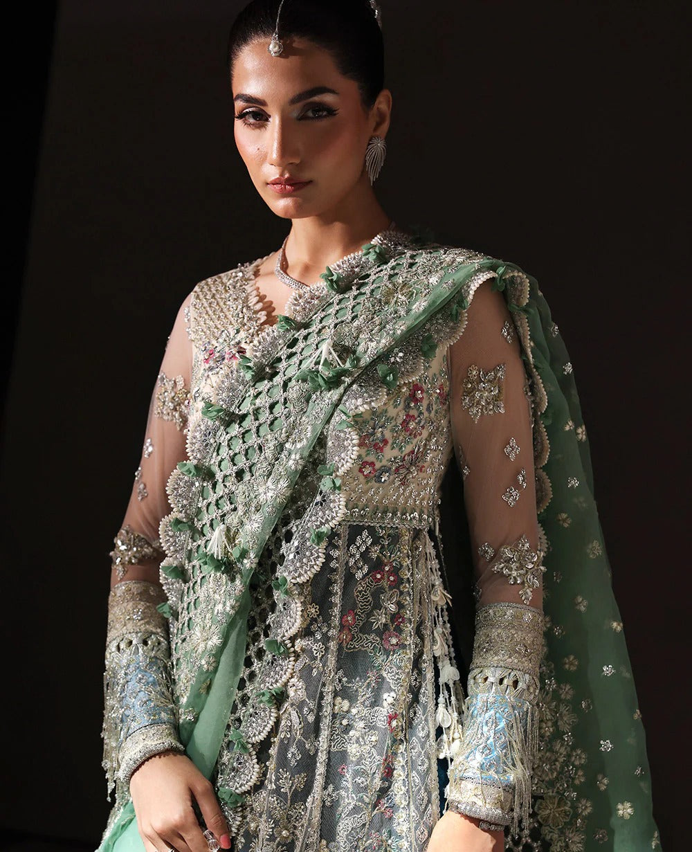 Woman wearing a traditional embroidered outfit with a green dupatta against a dark background