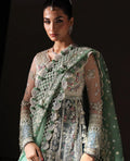 Woman wearing a traditional embroidered outfit with a green dupatta against a dark background