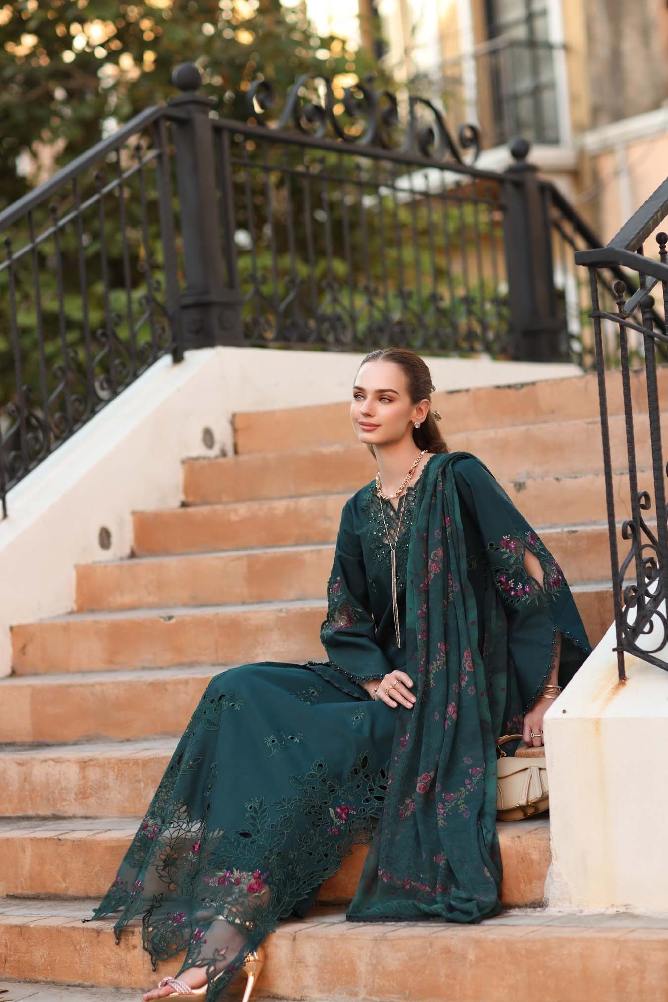 Woman in a dark green traditional outfit sitting on steps outdoors.