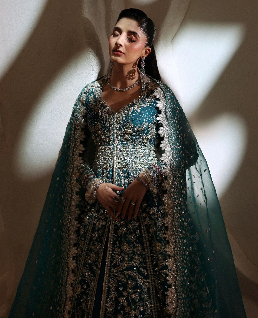 Woman in an ornate traditional outfit with intricate patterns, standing against a neutral background.