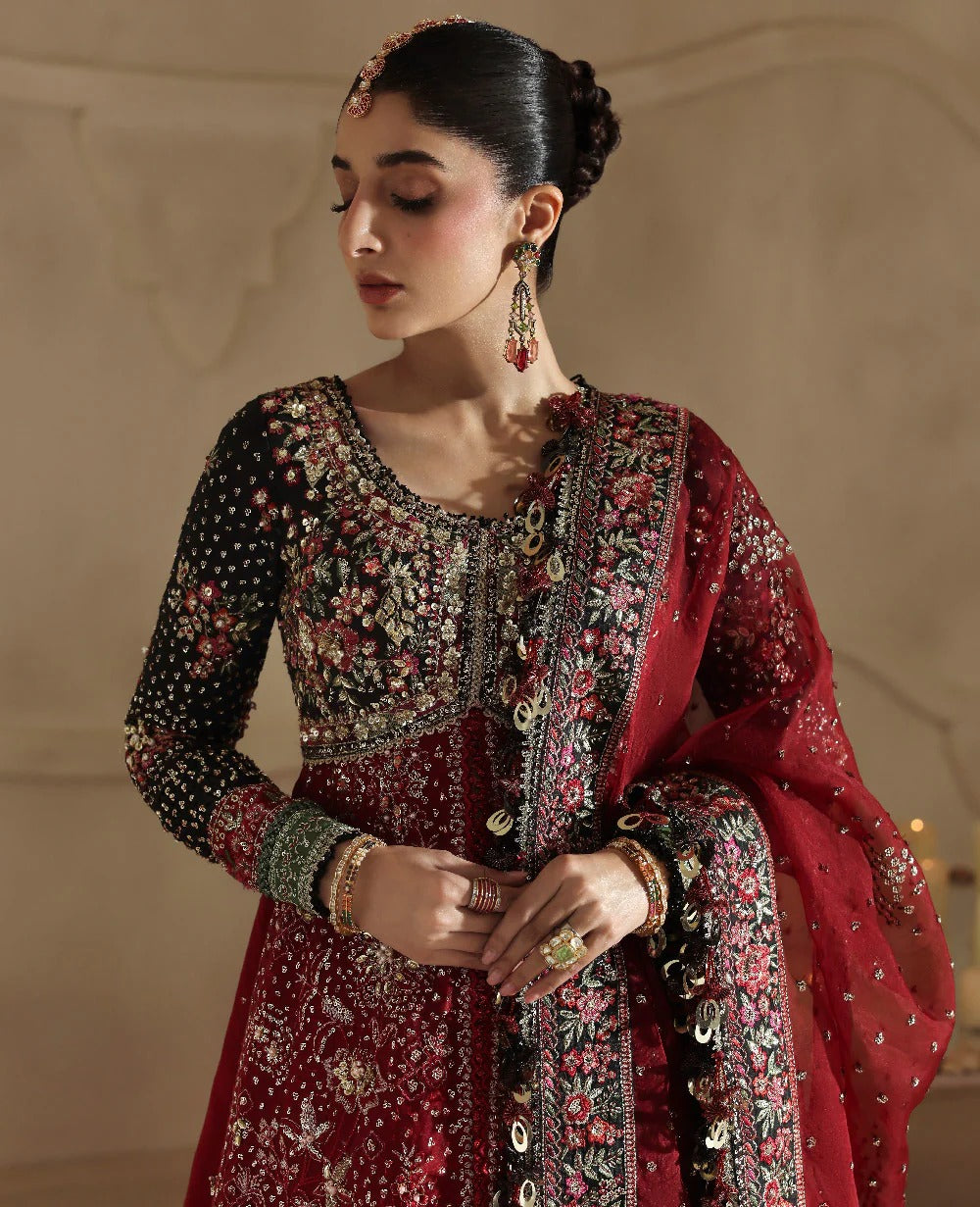 Woman in traditional embroidered outfit with red dupatta against a neutral background