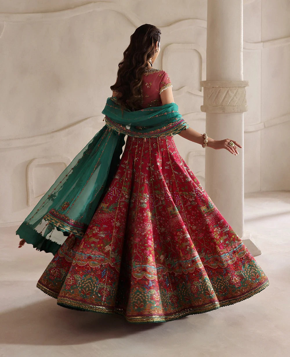 Woman in a traditional red and green outfit with floral patterns in an elegant setting.