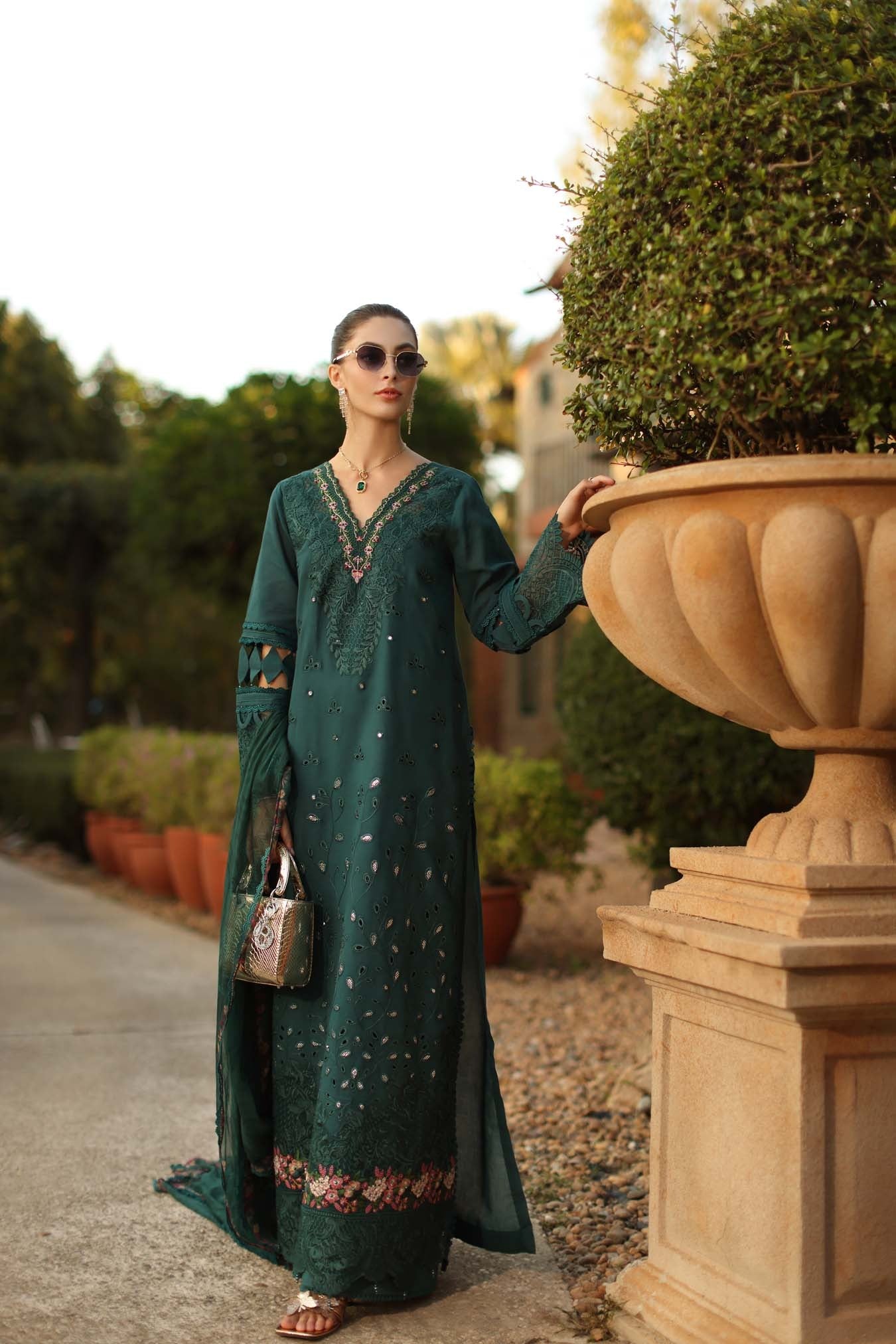 Woman in a long green dress standing next to a large decorative urn outdoors.