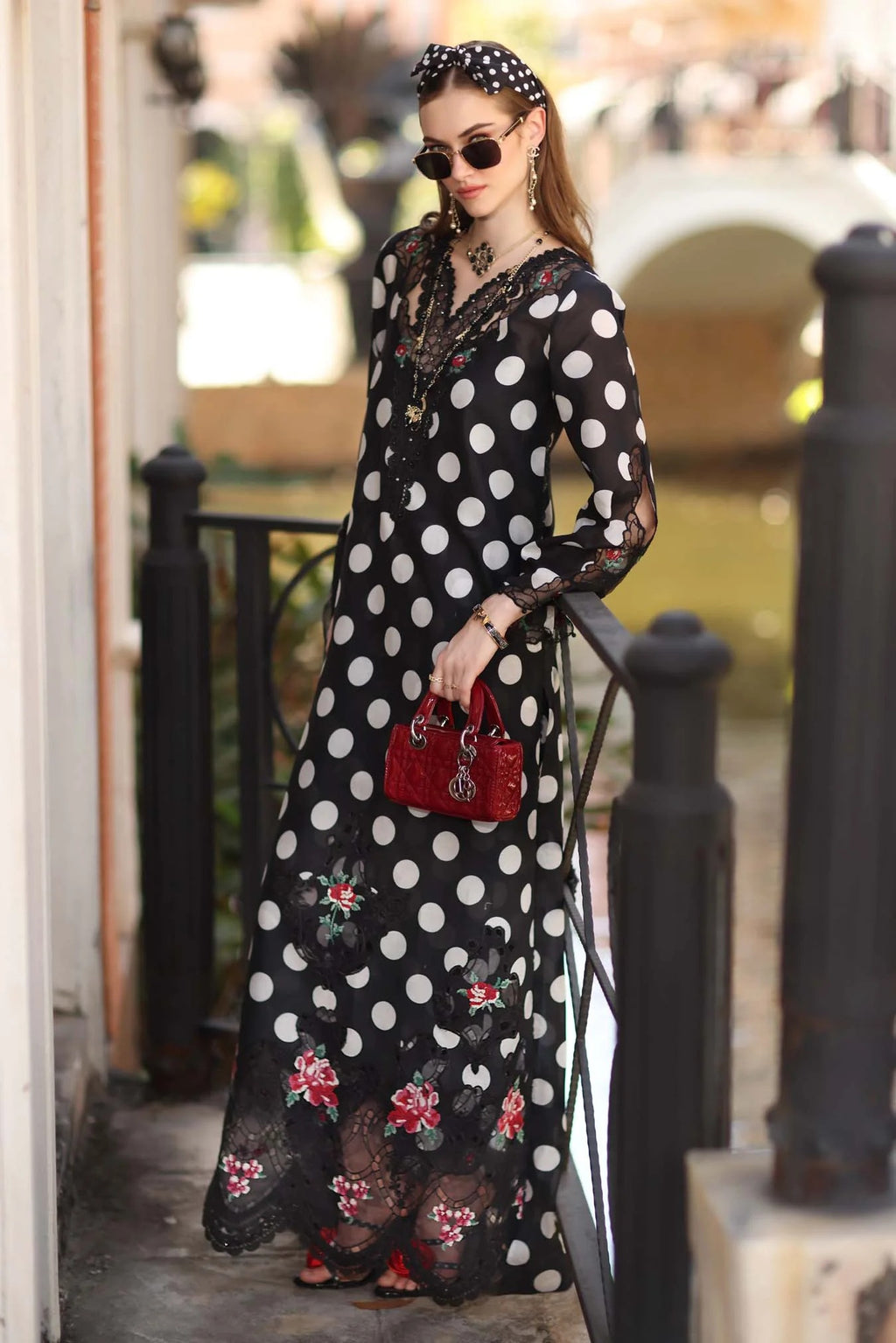 Woman in a black polka dot dress with floral details walking outdoors.