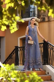 Woman in a blue traditional outfit standing on steps with greenery and a building in the background