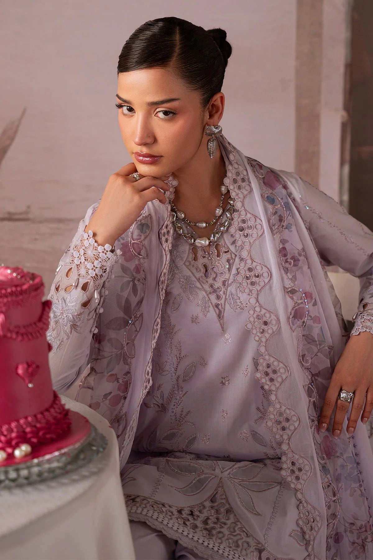 Woman in a floral outfit sitting next to a pink cake with heart decorations.