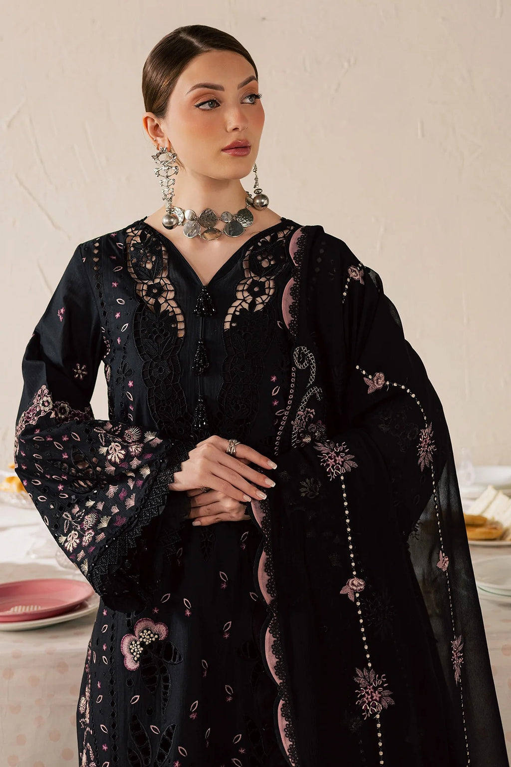 Woman wearing a black embroidered outfit with floral patterns on a neutral background