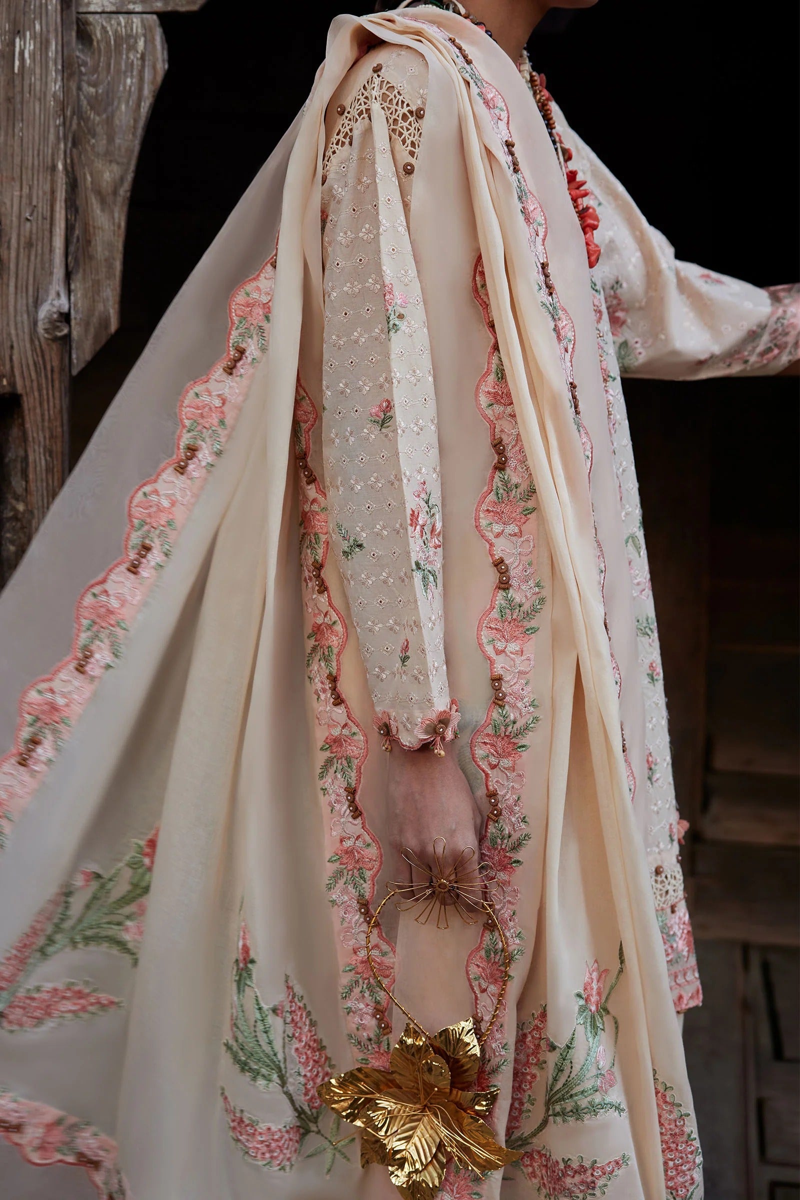 Close-up of a floral embroidered garment with a gold leaf accessory.