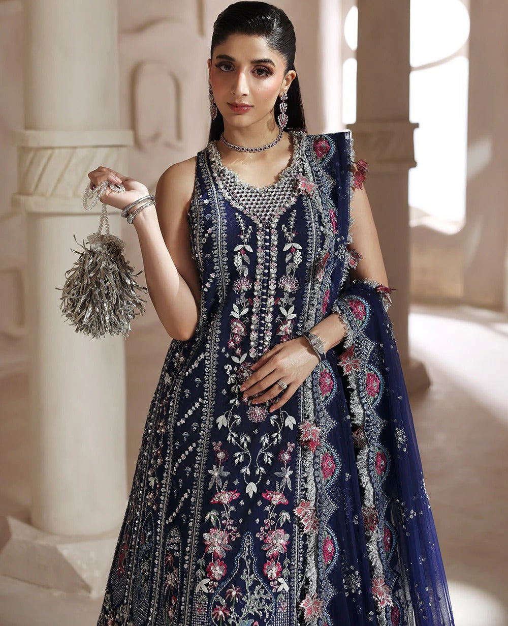 Woman in a dark blue embroidered traditional outfit holding a decorative bag in an elegant setting.