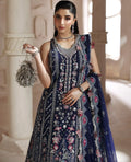 Woman in a dark blue embroidered traditional outfit holding a decorative bag in an elegant setting.