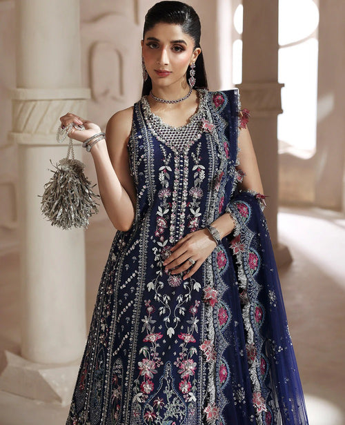 Woman in a dark blue embroidered traditional outfit holding a decorative bag in an elegant setting.