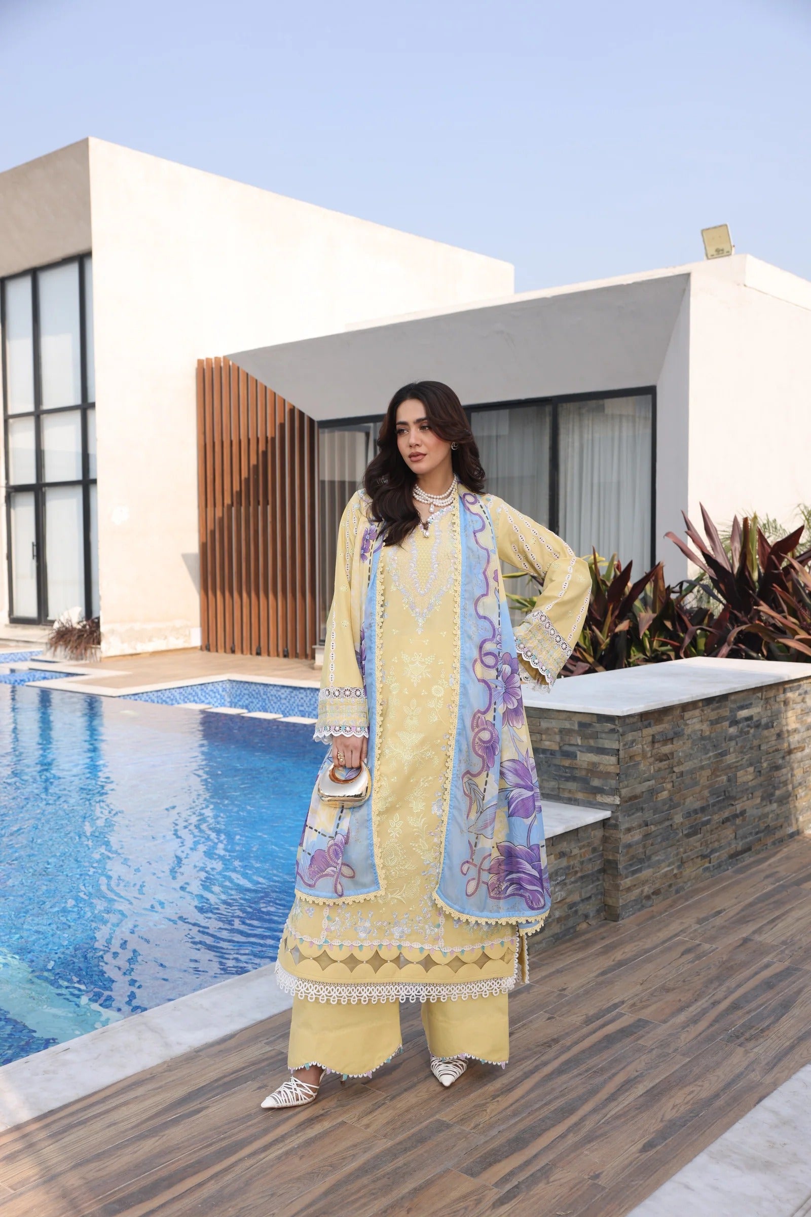 Woman in a yellow traditional outfit standing by a pool with a modern building in the background