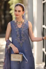 Woman in a blue embroidered dress holding a beige handbag with 'MOOR' branding.