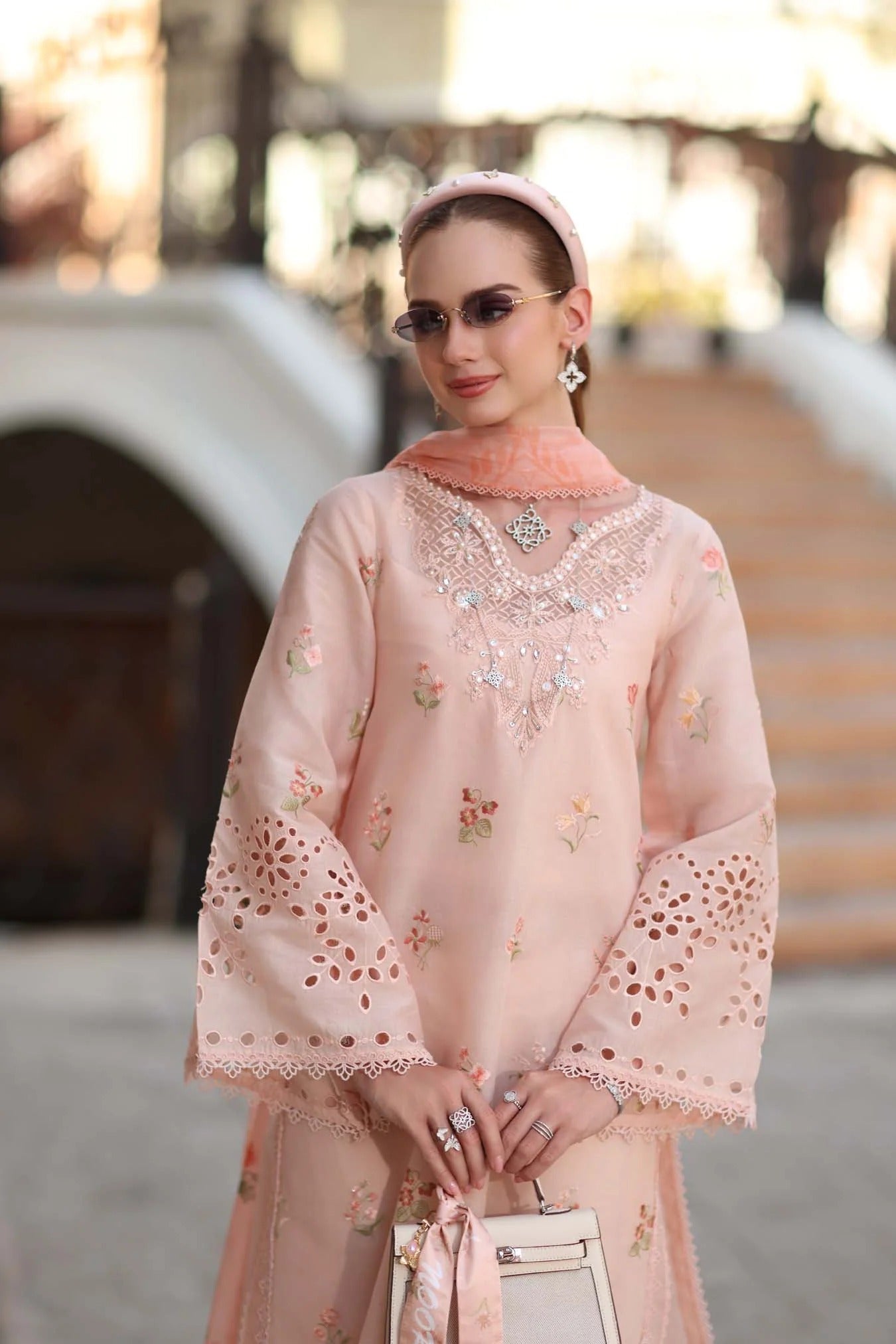 Woman wearing a light pink traditional outfit with floral patterns in an outdoor setting.