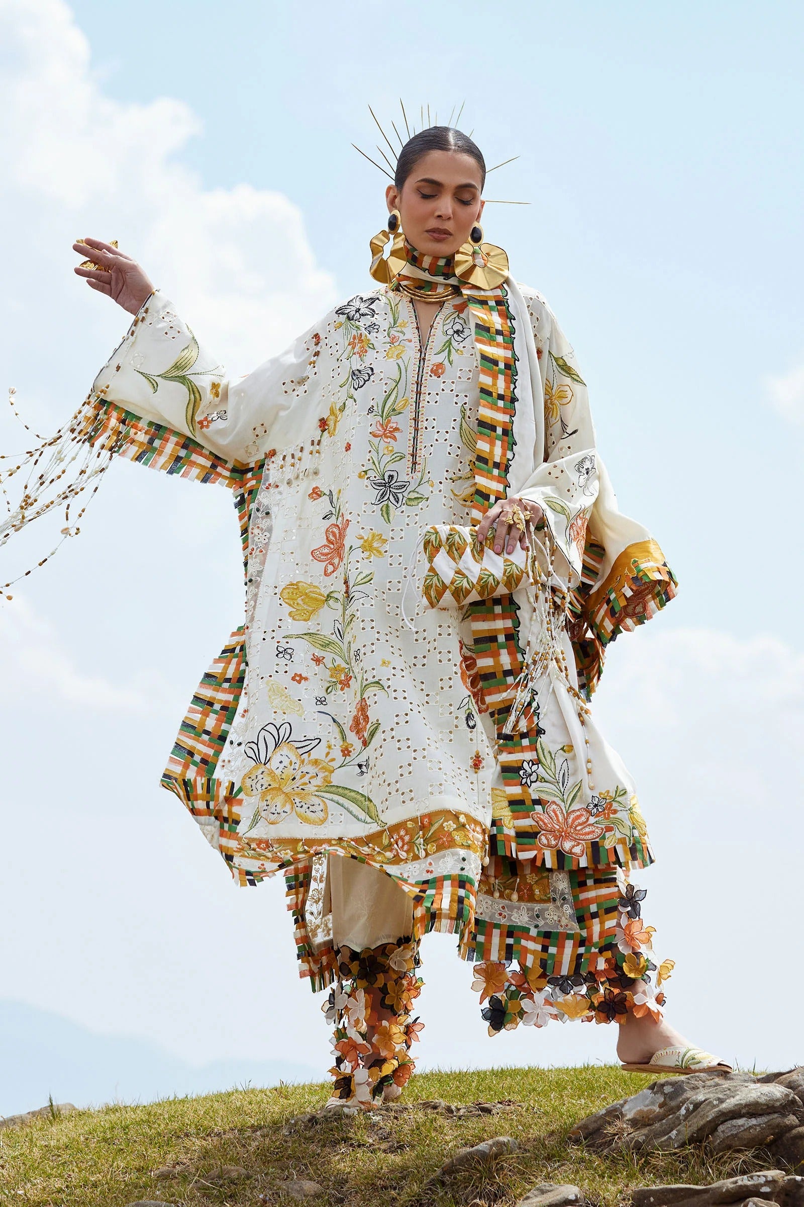 Person wearing a colorful embroidered outfit on a grassy hill with a blue sky.