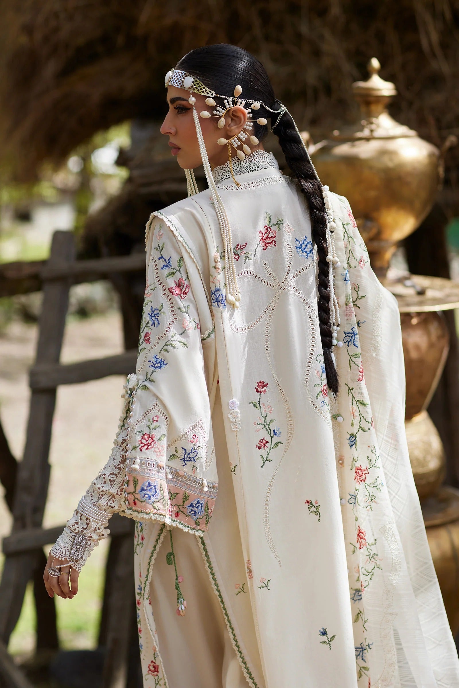 Woman in traditional embroidered outfit with decorative headpiece and jewelry, standing outdoors.