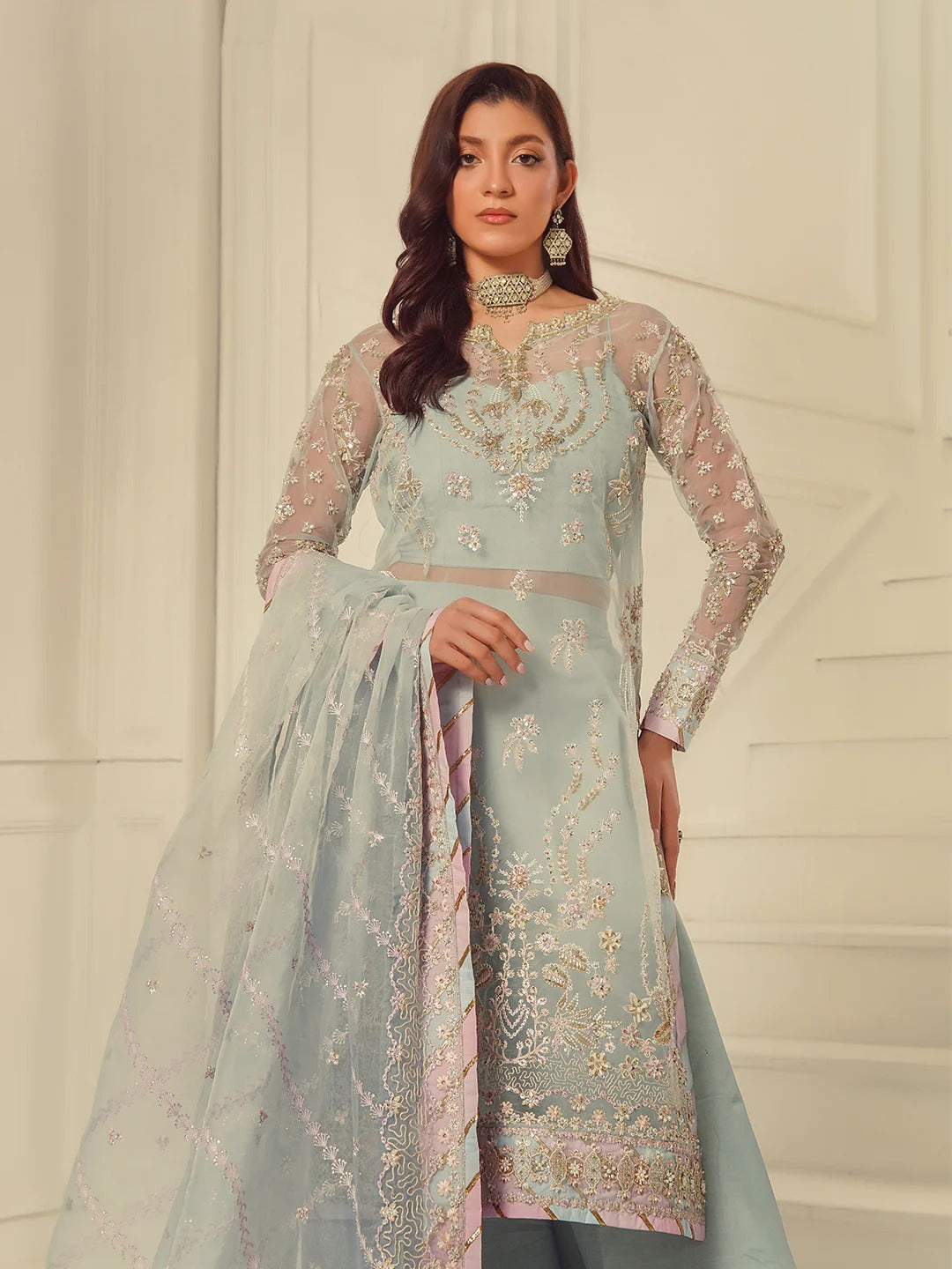 Woman wearing a light blue embroidered traditional outfit with a white background
