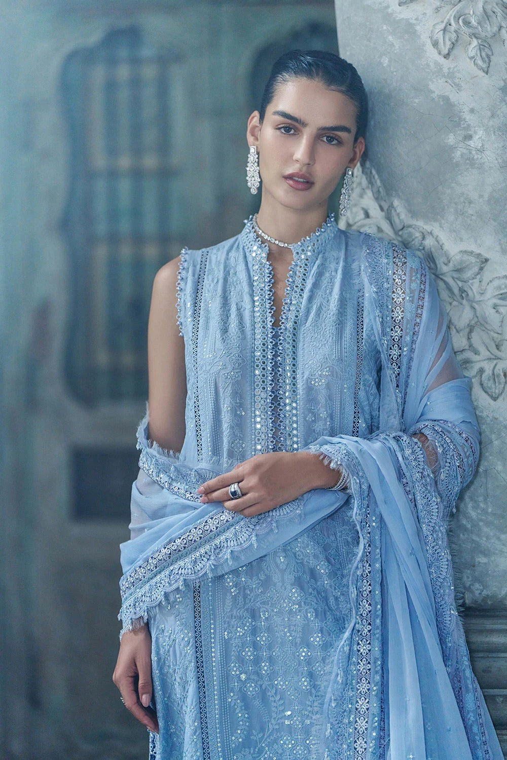 Woman wearing a light blue embroidered traditional outfit in an ornate interior setting.