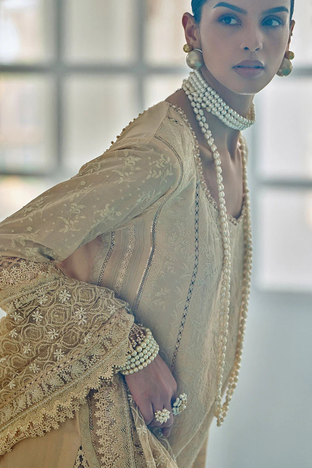 Woman in a traditional embroidered outfit with pearl jewelry against a blurred indoor background