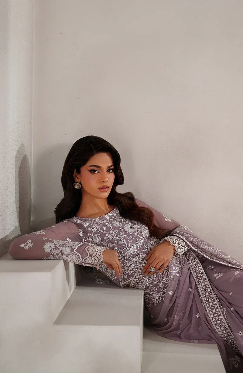Woman in a lavender traditional outfit with white patterns sitting on a white staircase.