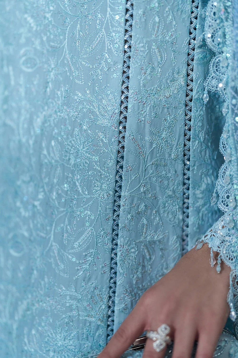 Close-up of a blue embroidered fabric with a hand holding a ring.