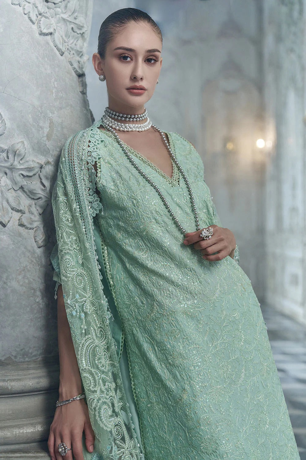 Woman wearing a light green saree with intricate patterns in an elegant indoor setting.