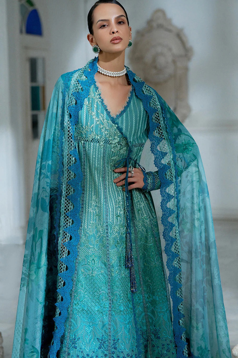 Woman wearing a turquoise embroidered dress with a matching shawl in an elegant indoor setting.