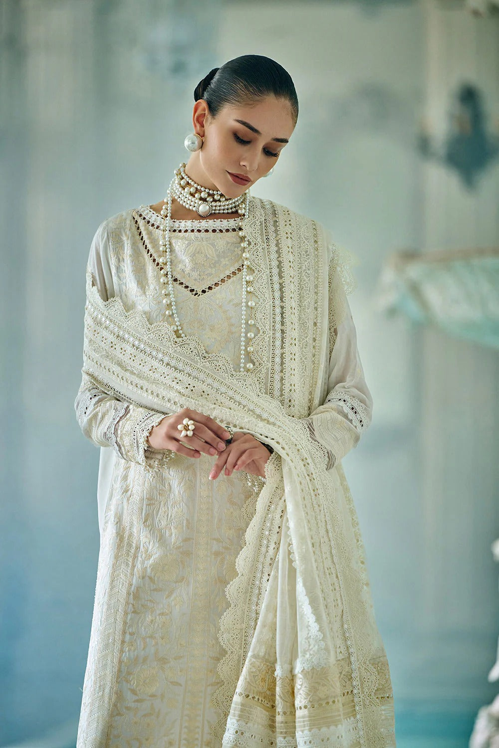 Woman in a white traditional outfit with intricate details and jewelry against a blurred background