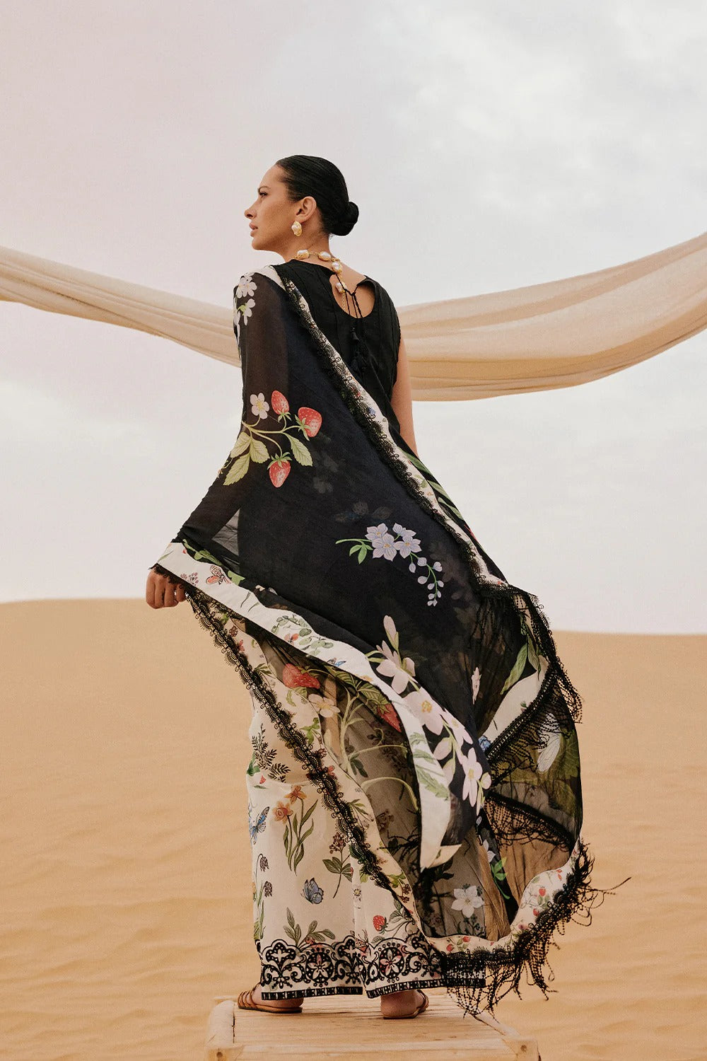 Woman in a black and white floral dress with a beige scarf in a desert setting
