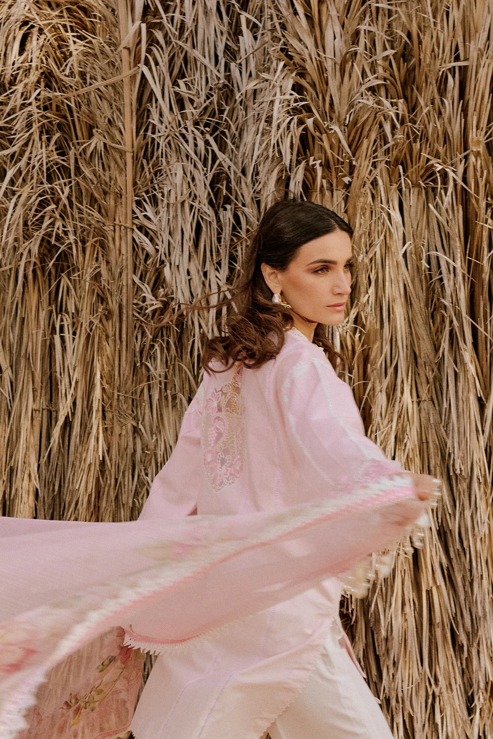 Woman in a pink dress standing against a natural, dried plant background
