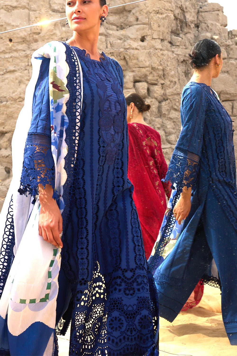 Woman wearing a blue lace dress with another person in a red outfit in the background.