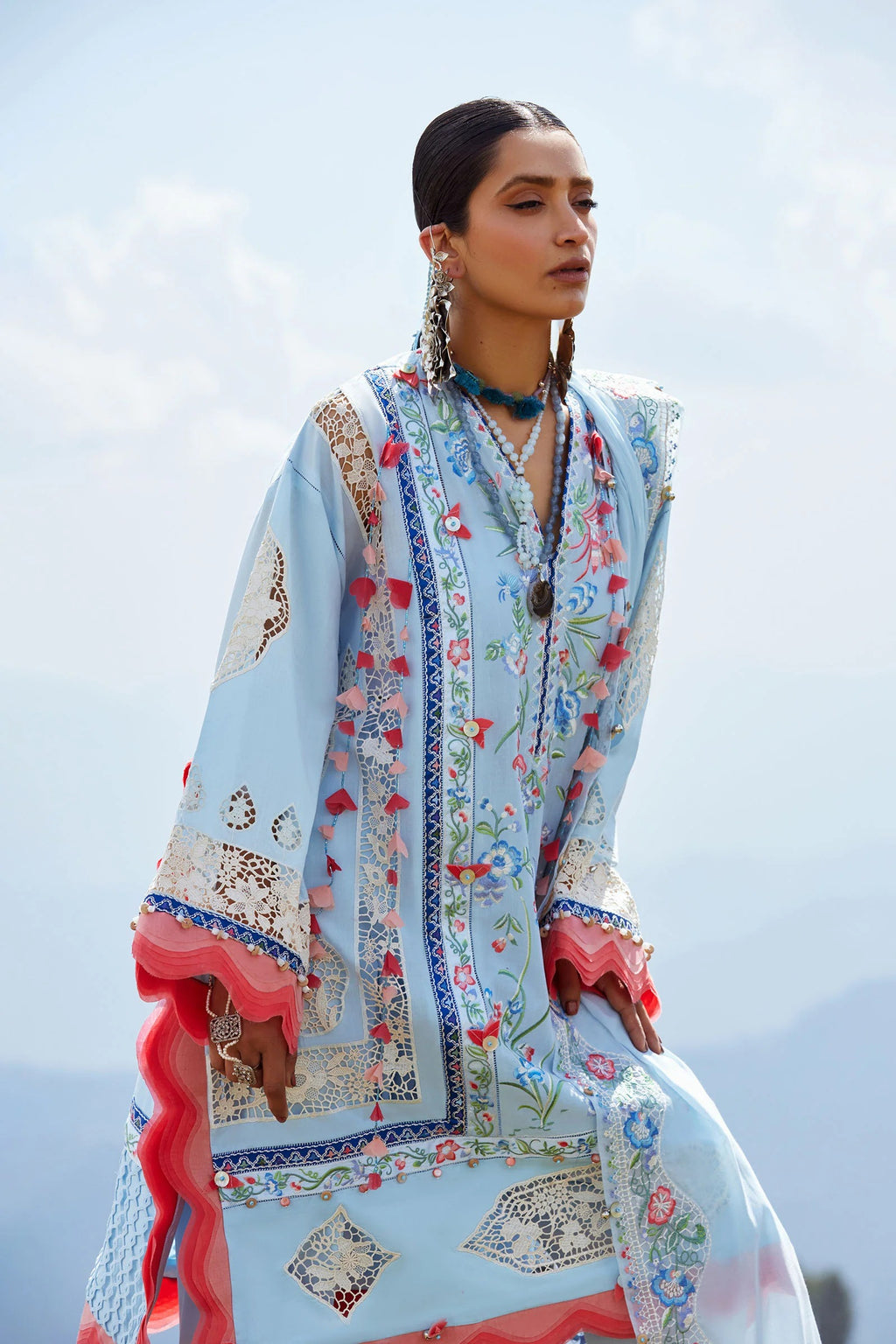 Woman wearing a light blue embroidered shawl with floral patterns against a clear sky.
