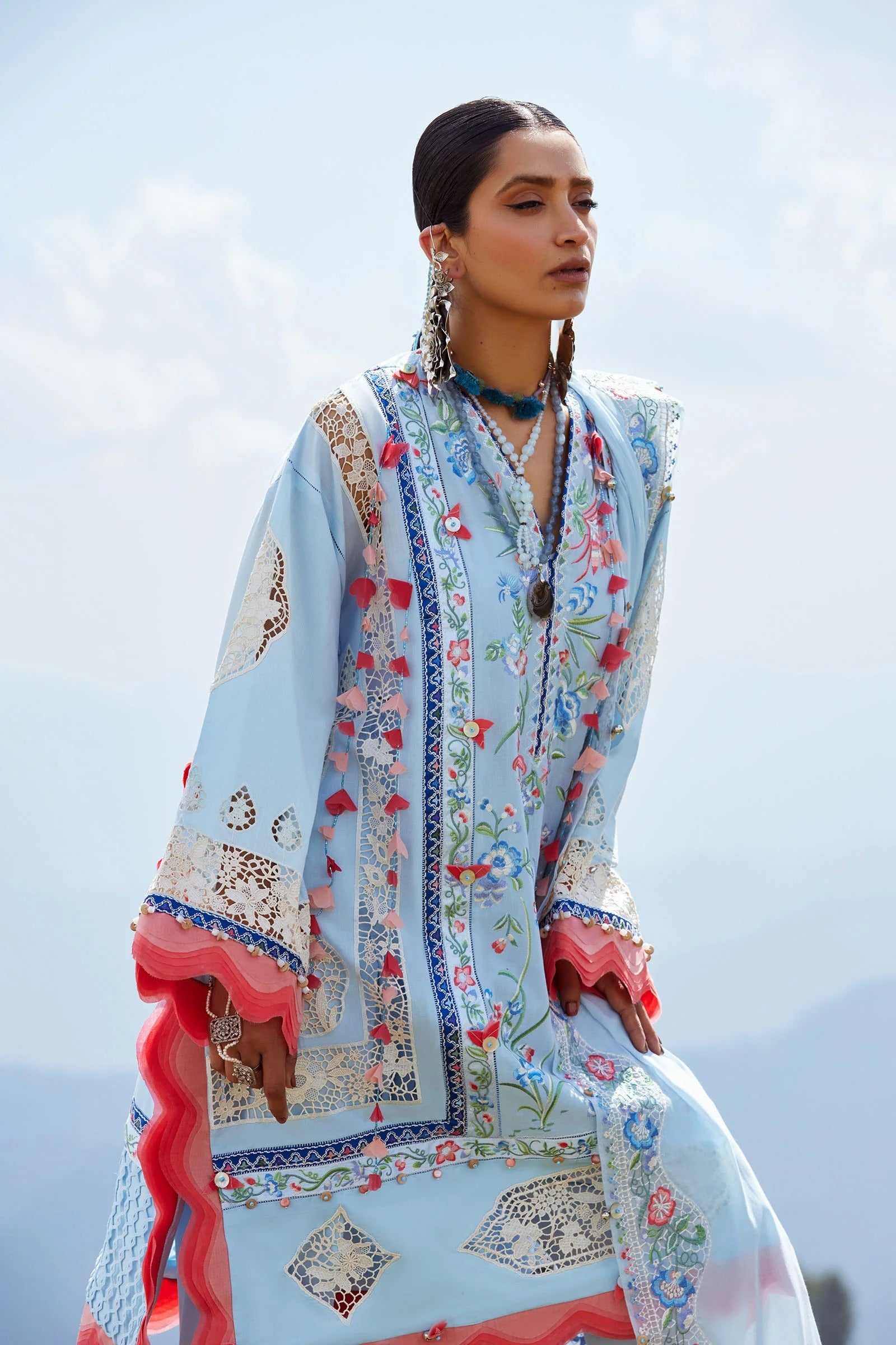Woman wearing a light blue embroidered shawl with floral patterns against a clear sky.