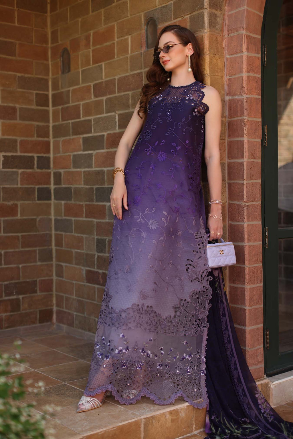 Woman in a long, elegant purple dress standing against a brick wall.