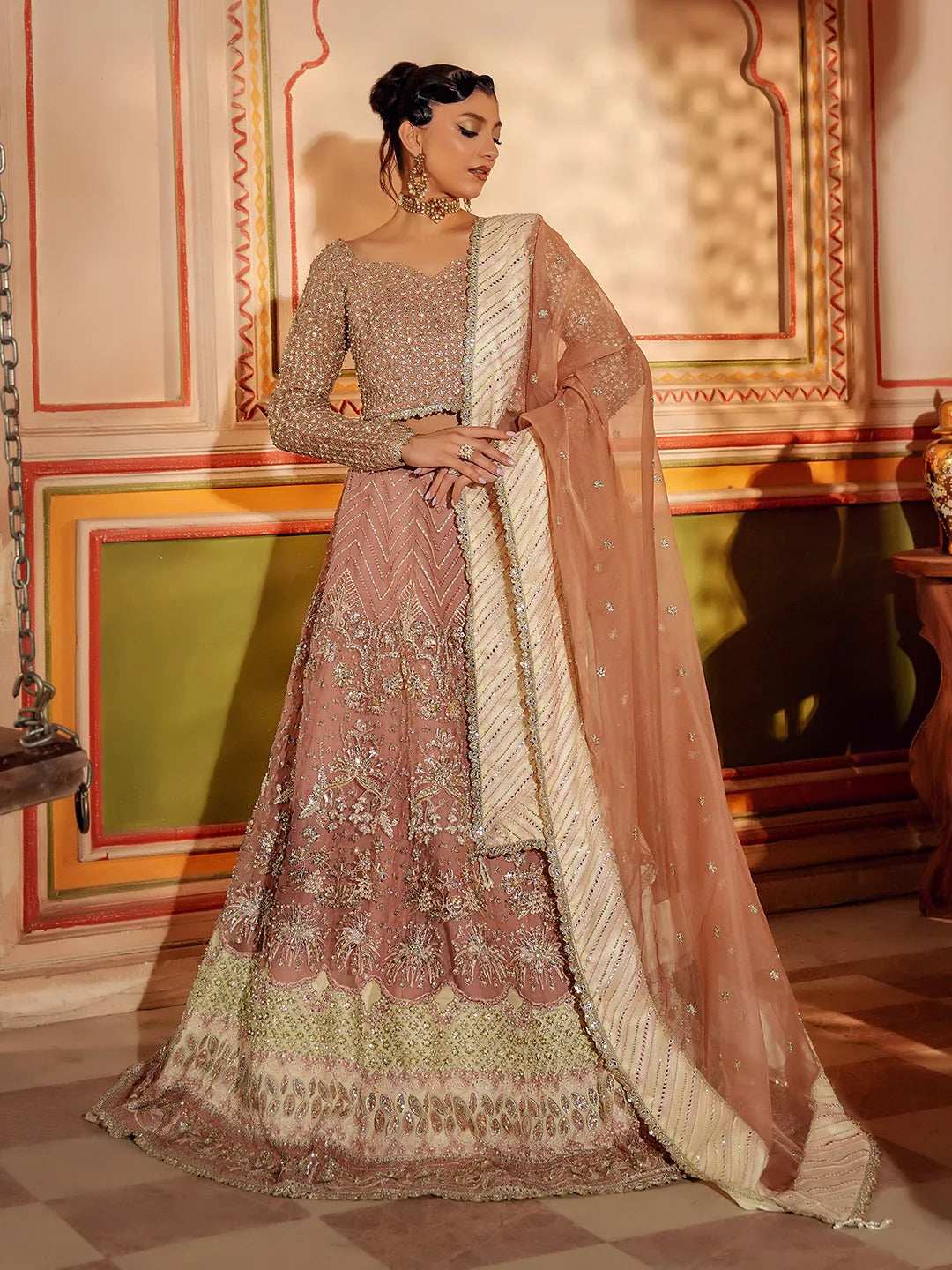 Woman in traditional embroidered pink and green outfit with dupatta in ornate indoor setting