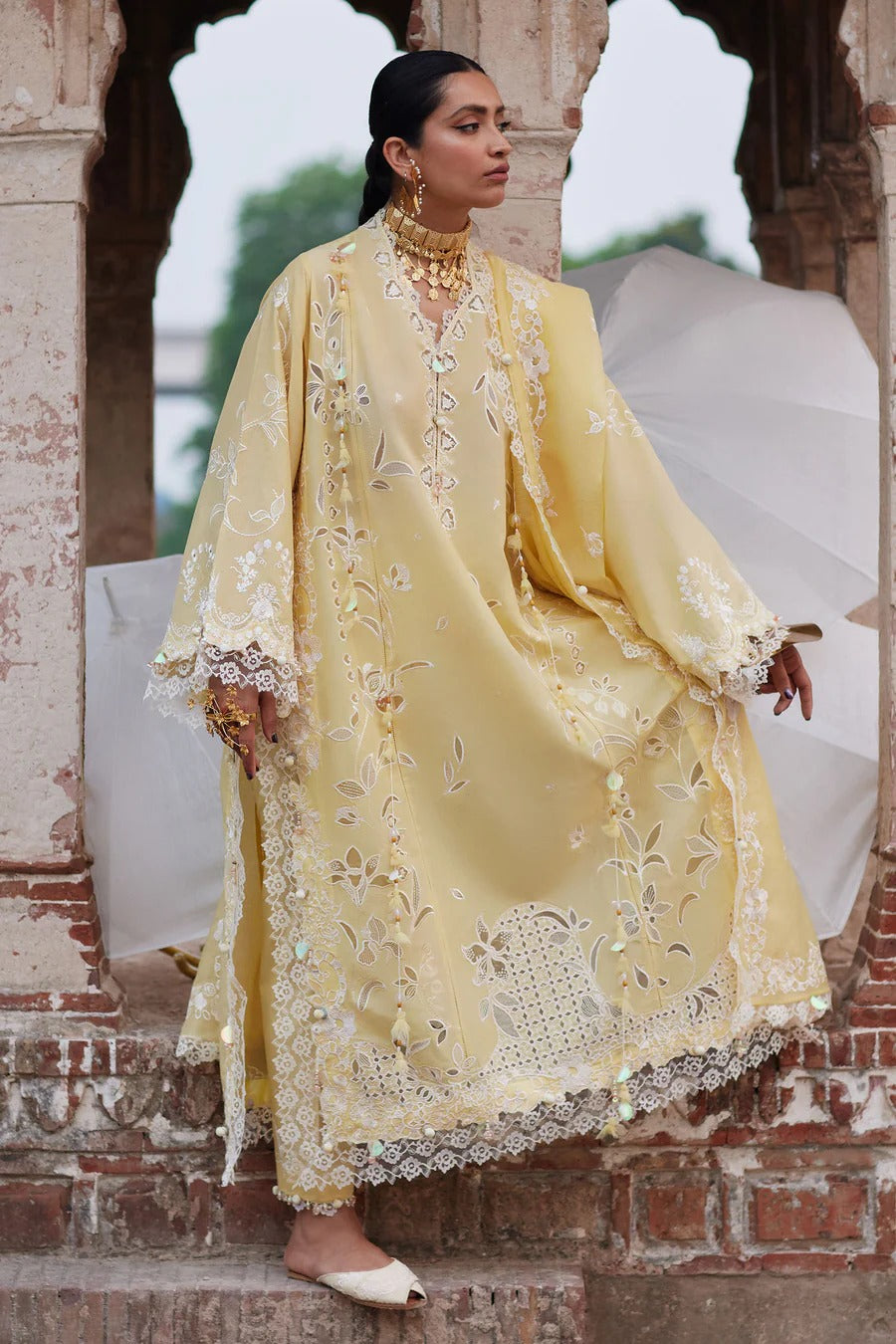 Woman in a yellow embroidered traditional outfit standing in front of an architectural structure.