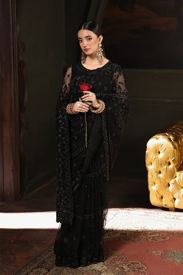 Woman in a black saree holding a red rose in a dimly lit room with a gold chair.