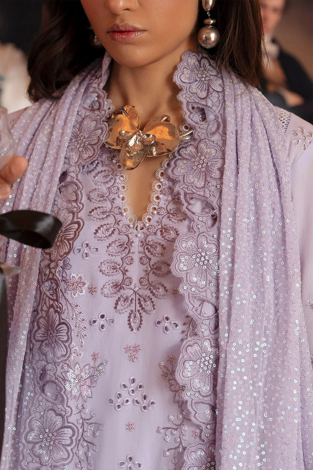 Woman wearing a light purple embroidered outfit with a matching scarf.